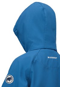 Blauwe waterdichte jas met capuchon, voorzien van een wit "Mammut" logo en een ronde patch met een zwarte mammoet op de linker mouw.