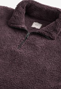 Fleece virsjakas tumši violetā krāsā ar augstu apkakli un priekšu ar rāvējslēdzēju. Strukturēta, mīksta auduma sastāvs, ar melnu rāvējslēdzēju un zīmola uzlīmi.