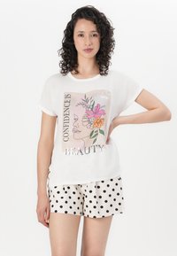 White short-sleeve top featuring a floral graphic with text and metallic accents, paired with polka dot shorts in beige and black.