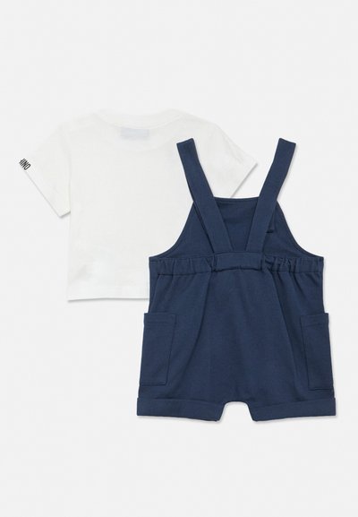 White short-sleeve shirt paired with navy blue short overalls featuring shoulder straps and front pockets, laid flat on a light background.