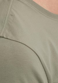 Olive green t-shirt with short sleeves, smooth cotton material, featuring subtle stitching details and a round neckline.