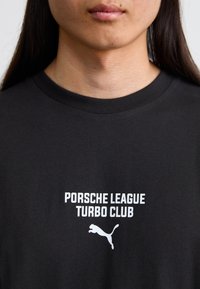 Sort bomuld T-shirt med hvid tekst "PORSCHE LEAGUE TURBO CLUB" og et springende Puma-logo. Rund hals design, glat tekstur.