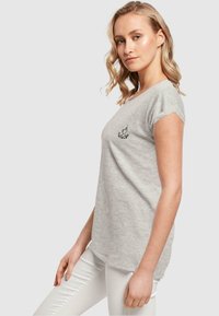 Hellgraues, kurzärmliges T-Shirt aus Baumwollmischung mit rundem Halsausschnitt und einem kleinen schwarzen Grafikdesign auf der Brust.