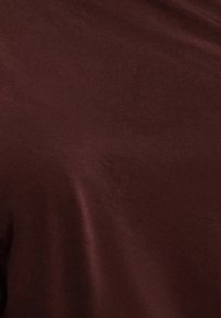 Vinrött tyg med en slät, glänsande textur och lätt glans, som draperar mjukt med subtila ljusvariationer. Inga mönster eller metalldetaljer syns.