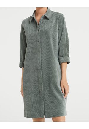 Sukienka koszulowa na długi rękaw, zapinana na guziki, wykonana z miękkiego zielono-szarego sztruksu, z podwiniętymi mankietami, noszona przez osobę na jednolitym jasnym tle.