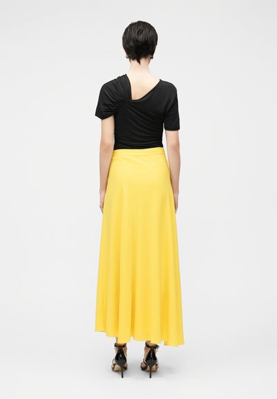 Haut noir à manches courtes avec une couture diagonale au dos, assorti d'une jupe maxi jaune fluide et de sandales noires à talons. Design épuré, texture lisse.