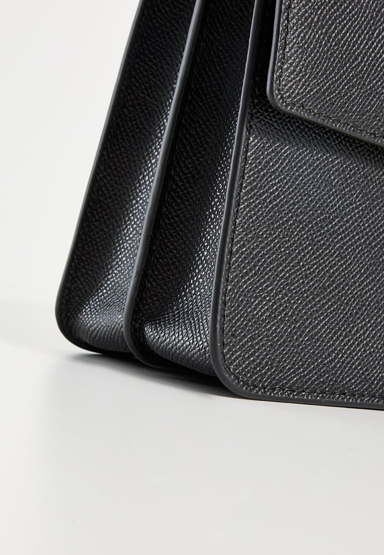 Schwarze Handtasche mit strukturiertem Design, glatten Kanten und einer klaren Form. Verfügt über ein dezentes Muster und einen Klappenverschluss. Das Material wirkt strapazierfähig.