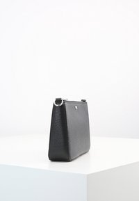 Sort læder håndtaske med en struktureret overflade, rektangulær form, lynlåslukning og sølvhardware-accenter på siden.