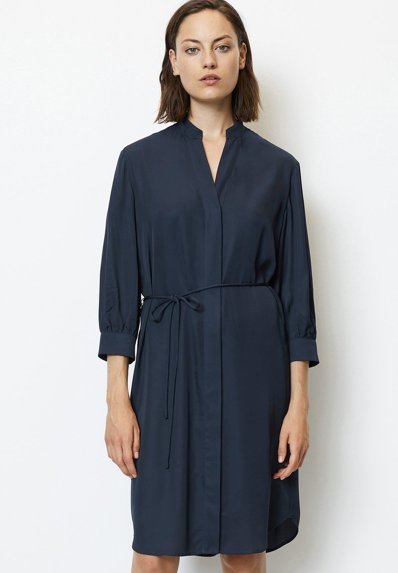 Abito blu navy realizzato in tessuto liscio, con colletto alla cinese, maniche tre quarti e vita con fiocco per una vestibilità regolabile.