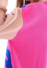 Färggad tröja med en rosa kropp, kontrasterande ljusbeige axel och livfulla blå detaljer, tillverkad av ett mjukt, texturerat stickat material.