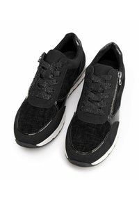 Černé tenisky s texturovanou tkaninou, třpytivými tkaničkami, bočními zipy a bílou gumovou podrážkou, zobrazené z šikmého horního pohledu na bílém pozadí.