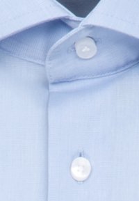 Col de chemise bleu clair et boutons supérieurs avec un gros plan sur la texture du tissu et les détails de la couture.