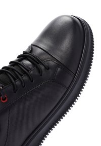 Scarpa in pelle nera con punta arrotondata, pannelli texturizzati, lacci neri e occhielli rossi, dotata di una spessa suola in gomma nera.