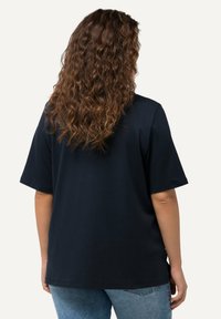 T-shirt in cotone blu navy con maniche corte, vestibilità comoda e texture liscia, mostrato da dietro con capelli ricci visibili.