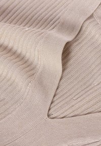 Tissu en tricot beige avec une texture côtelée, présentant des motifs variés et des accents lisses. Le tissu semble doux et élastique.
