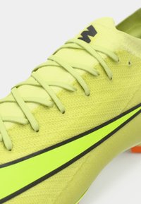 Pantofii sport de culoare galben aprins au un superior texturat, șireturi subțiri și un design cu dungi negre. Au un călcâi format și accente portocalii pe talpa exterioară.