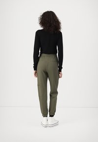 Joggers verde oliva con cintura elástica y puños ajustados, combinados con una camiseta negra de manga larga y zapatillas blancas de caña alta.