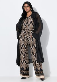 Zwart gestreepte jumpsuit met gouden accenten, gecombineerd met een lange doorzichtige zwarte jas. Heeft wijde benen en een V-hals ontwerp. Zwarte hakken en accessoires.