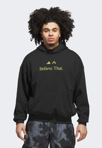 Sort hætte-trøje med en frontlomme, der har gul tekst "Believe That." og logo. Lavet af blødt stof med en afslappet pasform og snor i hætten.