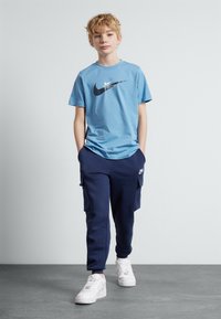 Gaišzilā kokvilnas T-kreklu ar melno Nike logo, apvienojot ar tumši ziliem cargo biksēm ar sānu kabatām un baltiem sneakeriem ar fakturētām zolēm.
