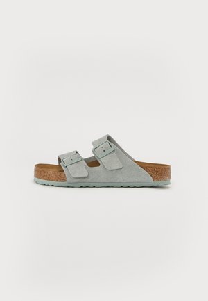 Lys grå ruskind slide sandal med to justerbare stropper, kork sål og struktureret gummisål. Minimalistisk design og flad profil.