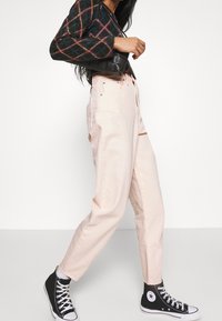 Pantalones de tiro alto en rosa claro con un ajuste relajado, que cuentan con bolsillos laterales y una costura ligera, combinados con zapatillas altas de lona negras.
