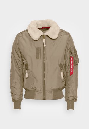 Beige bombázódzseki műszőrme gallérral, bordázott mandzsettákkal és aljjal. Cipzáros zsebekkel és piros címkével rendelkezik az ujján. Simább textúra.