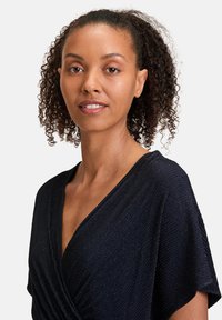 Marineblaues Kleid mit kurzen Ärmeln, V-Ausschnitt und strukturierter Stoffoberfläche mit dezenten Streifen. Glattes, fließendes Material mit einem sanften Glanz.