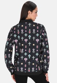 Jachetă bomber neagră, cu un model floral și geometric colorat, guler și manșete striate, dintr-un material neted și texturat.