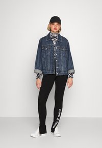 Denim oversized jacket, striped turtleneck, black ribbed leggings with logo, black cap, and white sneakers. Casual urban outfit.