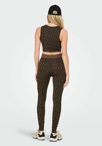 Brązowy crop top w Panterkę połączony z dopasowanymi legginsami. Ubranie charakteryzuje się dopasowanym krojem i miękką teksturą, noszone z czarnymi sneakersami.