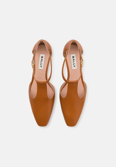 Pruunist nahast slingback kingad terava varbaga, lõigatud disainiga ja kuldse tooniga tõmblukuga aktsendiga. Sile tekstuur ja minimaalne detailitus.