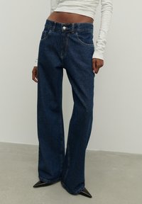 Laiad sinised teksad kõrge vöökohaga, ees taskud ja peene tekstuuriga. Kombineeritud terava ninaga mustade kontsakingadega.