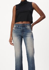 Svart ärmlös crop top parat med ljus tvätt, något förstörda vida jeans med fem fickor och knappgylf.