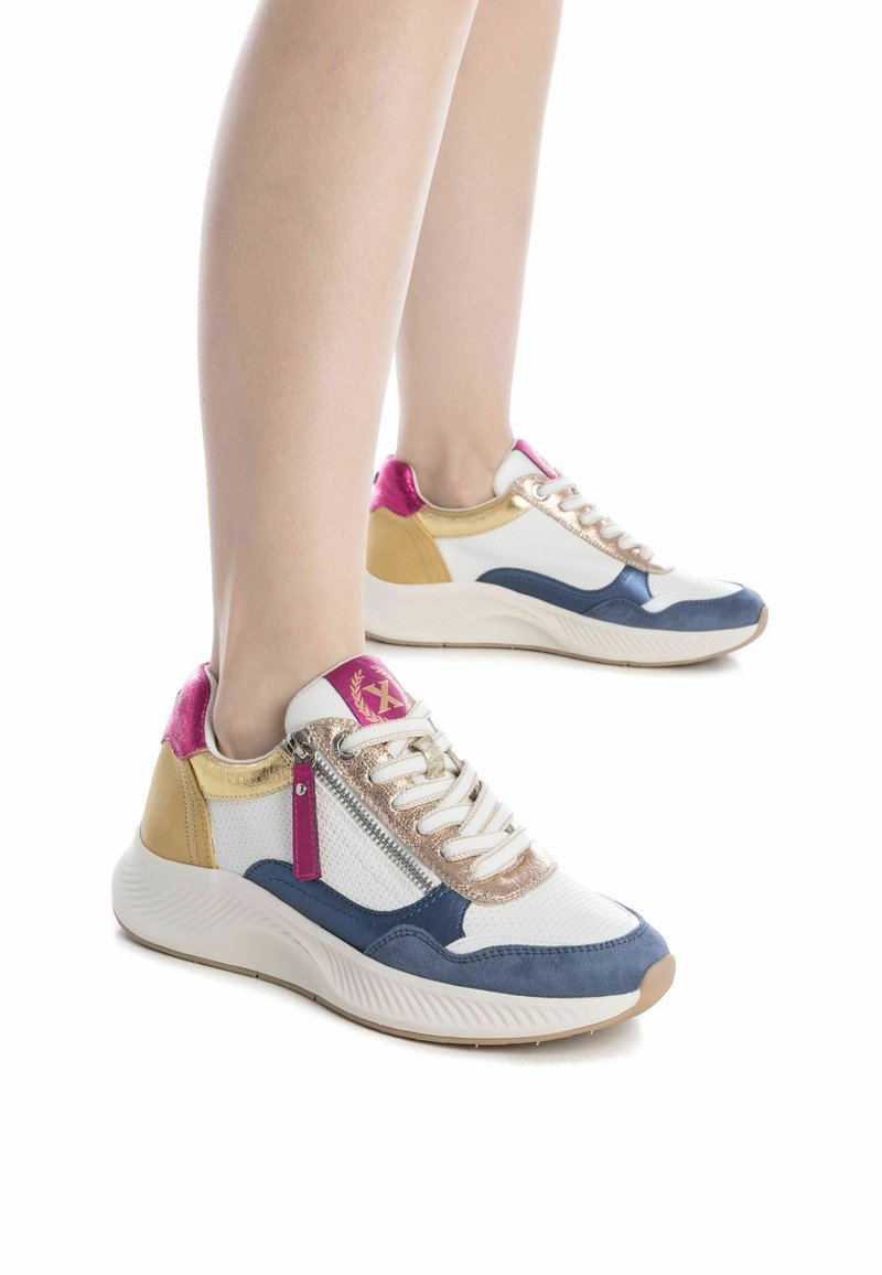 Zapatillas multicolores que combinan materiales en blanco, azul marino, dorado y rosa. El diseño incluye una parte superior texturizada y una cremallera lateral prominente.