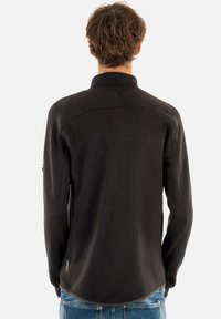 Sudadera de forro polar negra con cuello alto, corte ajustado y detalles de costura en la parte posterior. La tela tiene una textura suave y un acabado blando.