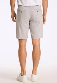 Lichtgrijze shorts met een gestructureerde stof, standaardzakken en subtiele stiksels, gecombineerd met witte sneakers.
