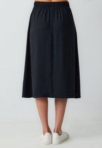 Jupe noire longueur cheville avec une taille élastique et une texture lisse et légère. Associée à des baskets blanches pour un look décontracté.