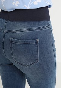 Mörkblå denimjeans med en ribbad marinblå midja, med detaljer på bakfickorna och subtila sömnadsaccenter. Slät textur och figurnära passform.