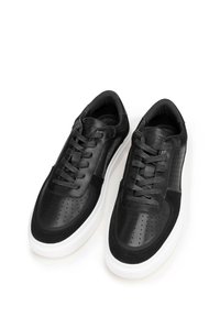 Černé tenisky s kombinací kůže a semiše, s perforovanými detaily, šněrováním a bílou gumovou podrážkou.