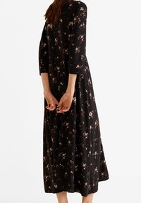 Robe noire à fleurs avec manches trois-quarts, longueur midi fluide, présentant un délicat motif floral multicolore, tissu léger et encolure arrondie.