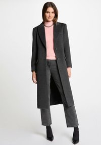 Abrigo largo de lana gris oscuro con una silueta entallada, que presenta dos botones, bolsillos laterales y un cuello con muescas, combinado con un suéter rosa.