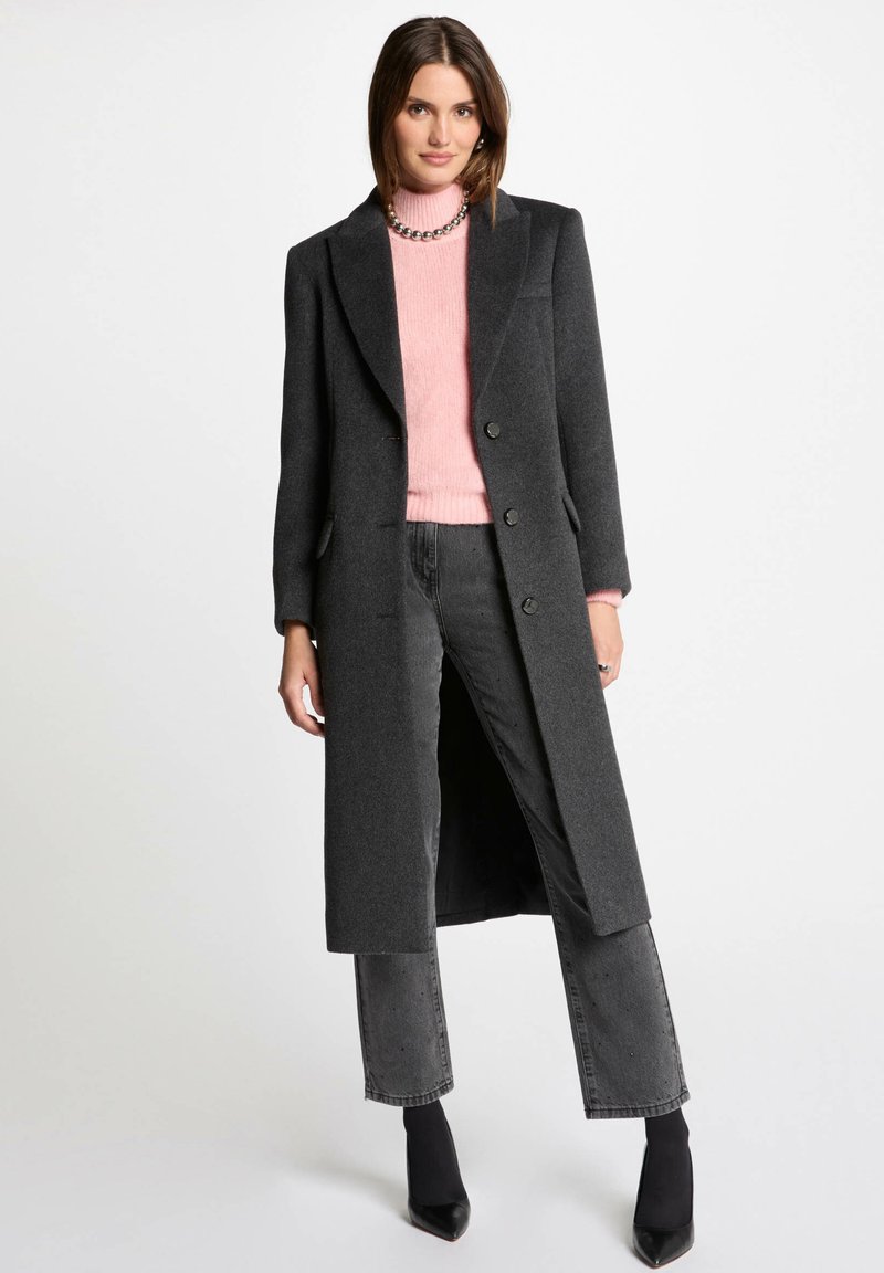 Abrigo largo de lana gris oscuro con una silueta entallada, que presenta dos botones, bolsillos laterales y un cuello con muescas, combinado con un suéter rosa.