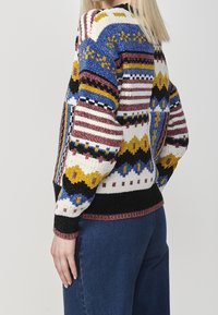 Maglione lavorato a maglia con motivi audaci in blu, giallo, marrone e nero. Vestibilità comoda con polsini e orlo a coste. Tessuto strutturato.