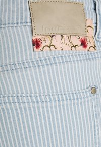 Tecido listrado azul claro, com um patch de couro bege e um tecido com padrão floral à vista do bolso. Inclui detalhe de botão de metal.