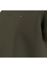 Polo w kolorze oliwkowym, wykonany z teksturowanej tkaniny, z krótkimi rękawami, kołnierzykiem i małym logo marki na lewej piersi.
