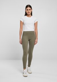 Witte cropped t-shirt met korte mouwen gecombineerd met olijfgroene leggings. Het model draagt witte sneakers met groene accenten.