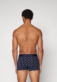 Boxers ajustados de color navy con un patrón repetido de logotipos en blanco, cinturilla elástica y diseño ceñido, mostrados desde la parte de atrás.
