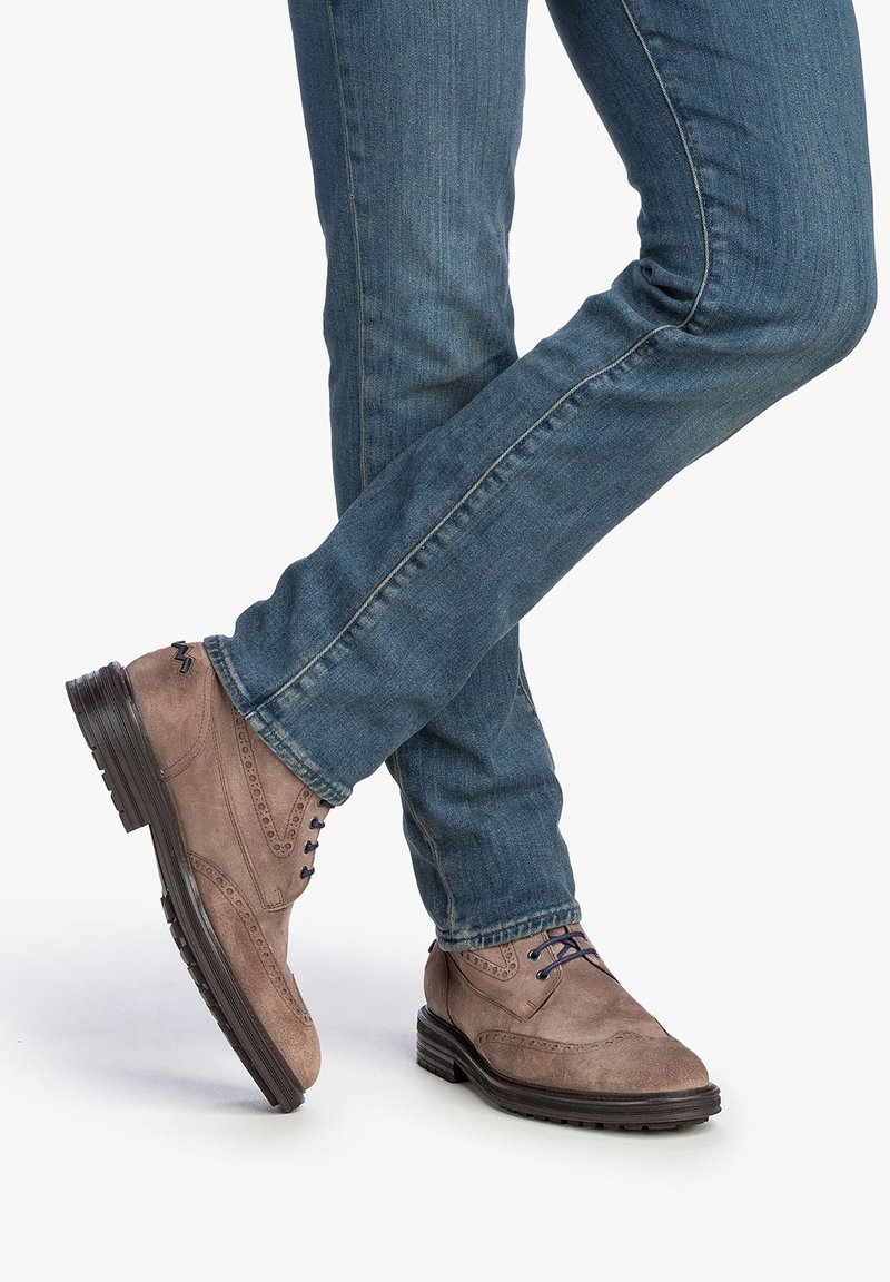 Chaussures en daim brun clair avec des détails brogue, bout rond et semelle plate foncée, associées à un jean en denim bleu.