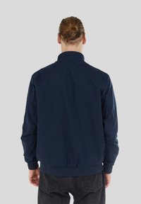 Marinblå bomberjacka med ribbad krage och mudd, med dragkedja fram och elastisk nederkant, tillverkad av ett lätt tyg.